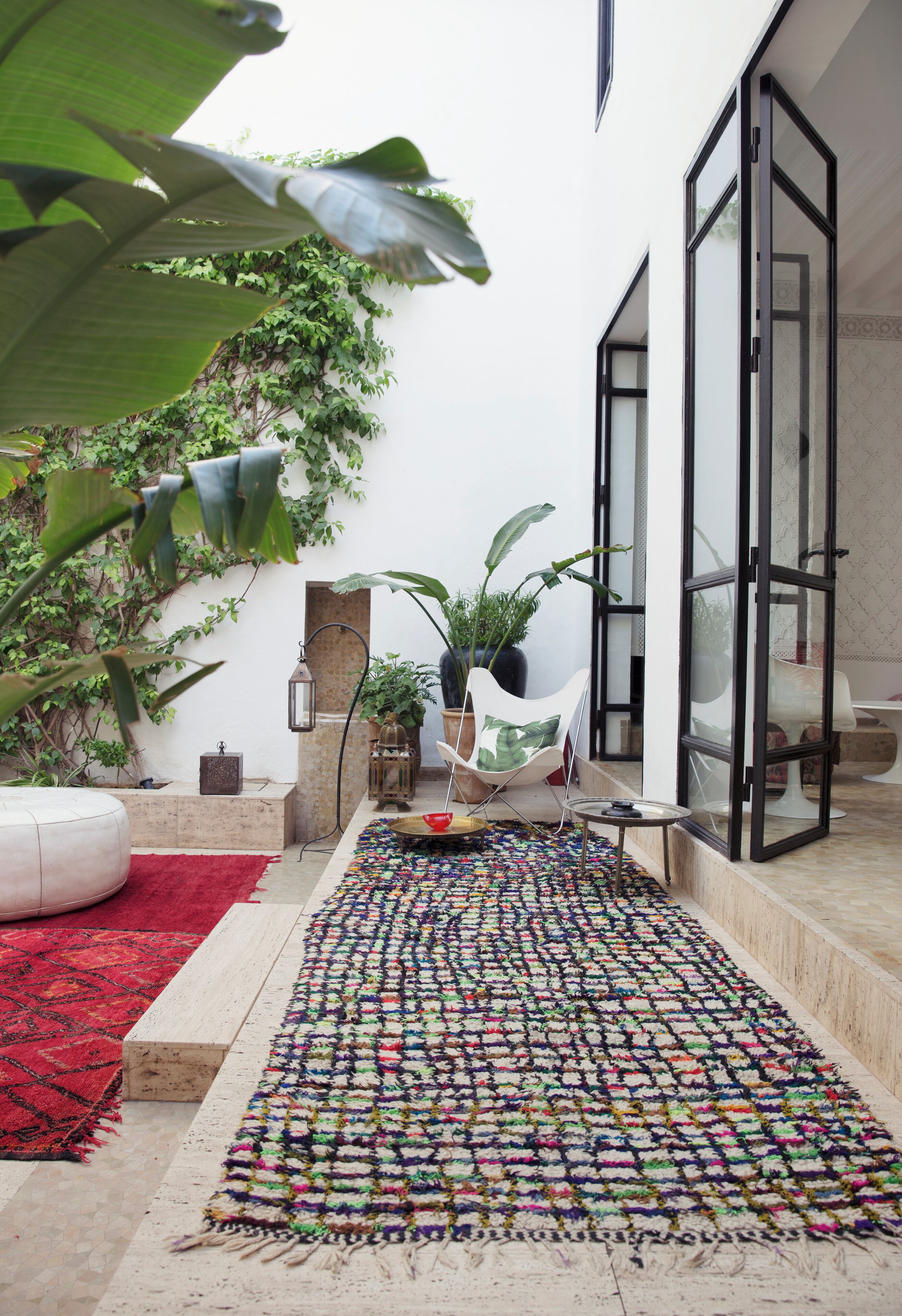 Un espace extérieur moderne agrémenté d’un tapis coloré à motifs tissés, d’un tapis rouge et d’une chaise blanche.