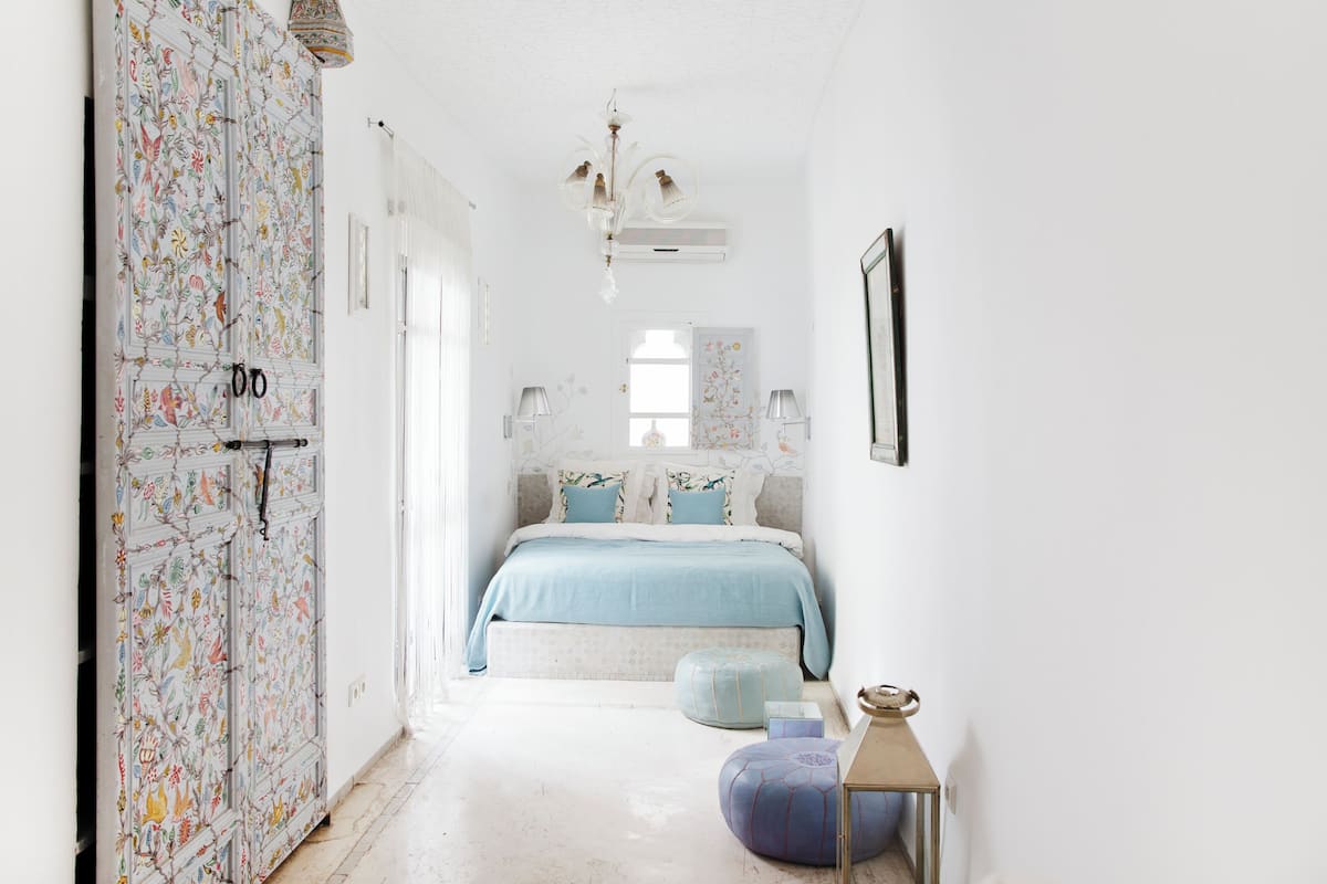 A bedroom with a bed, a nightstand, a chair, and a window.