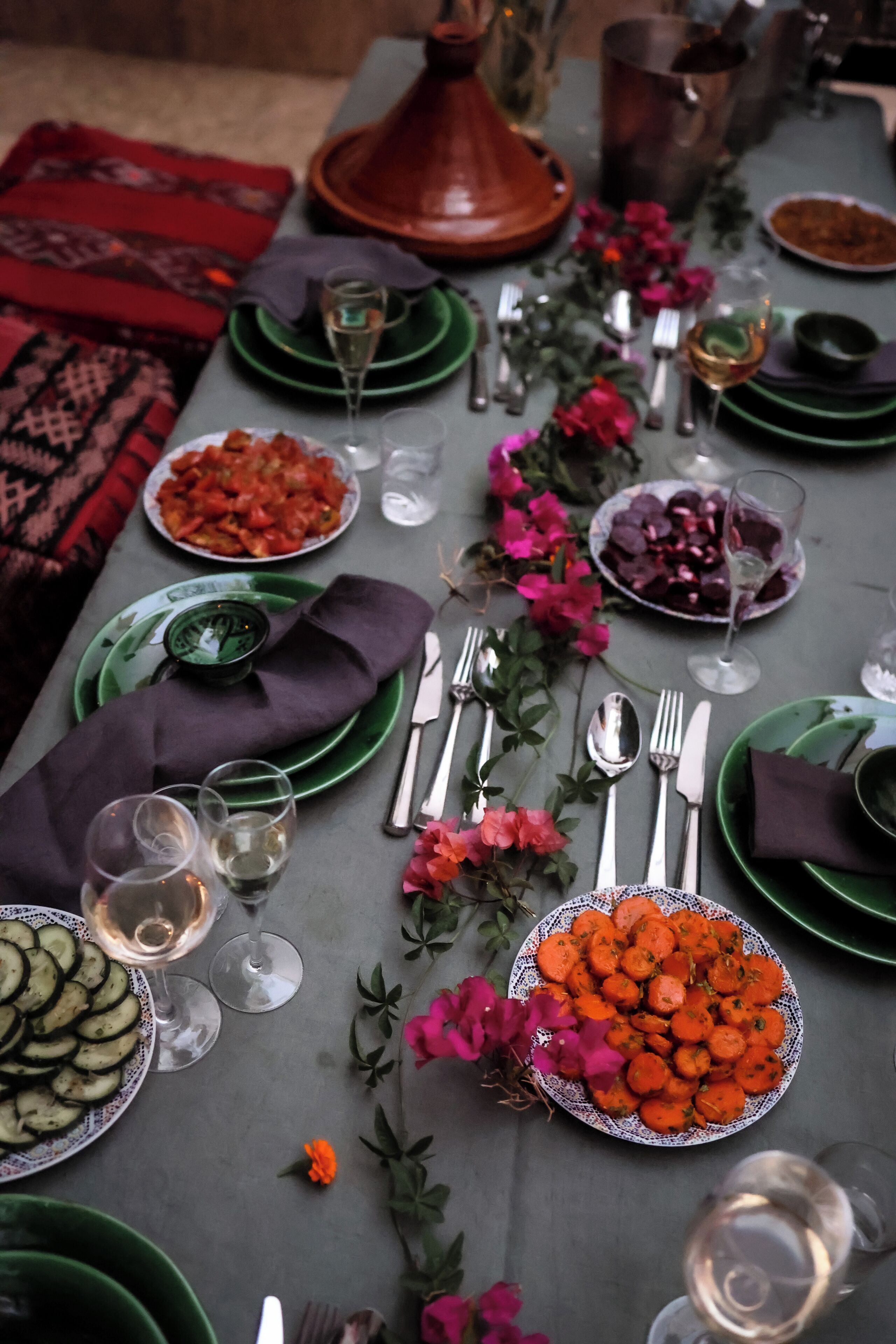 A table set for a meal with various dishes, glasses of wine, and a traditional Moroccan tagine.