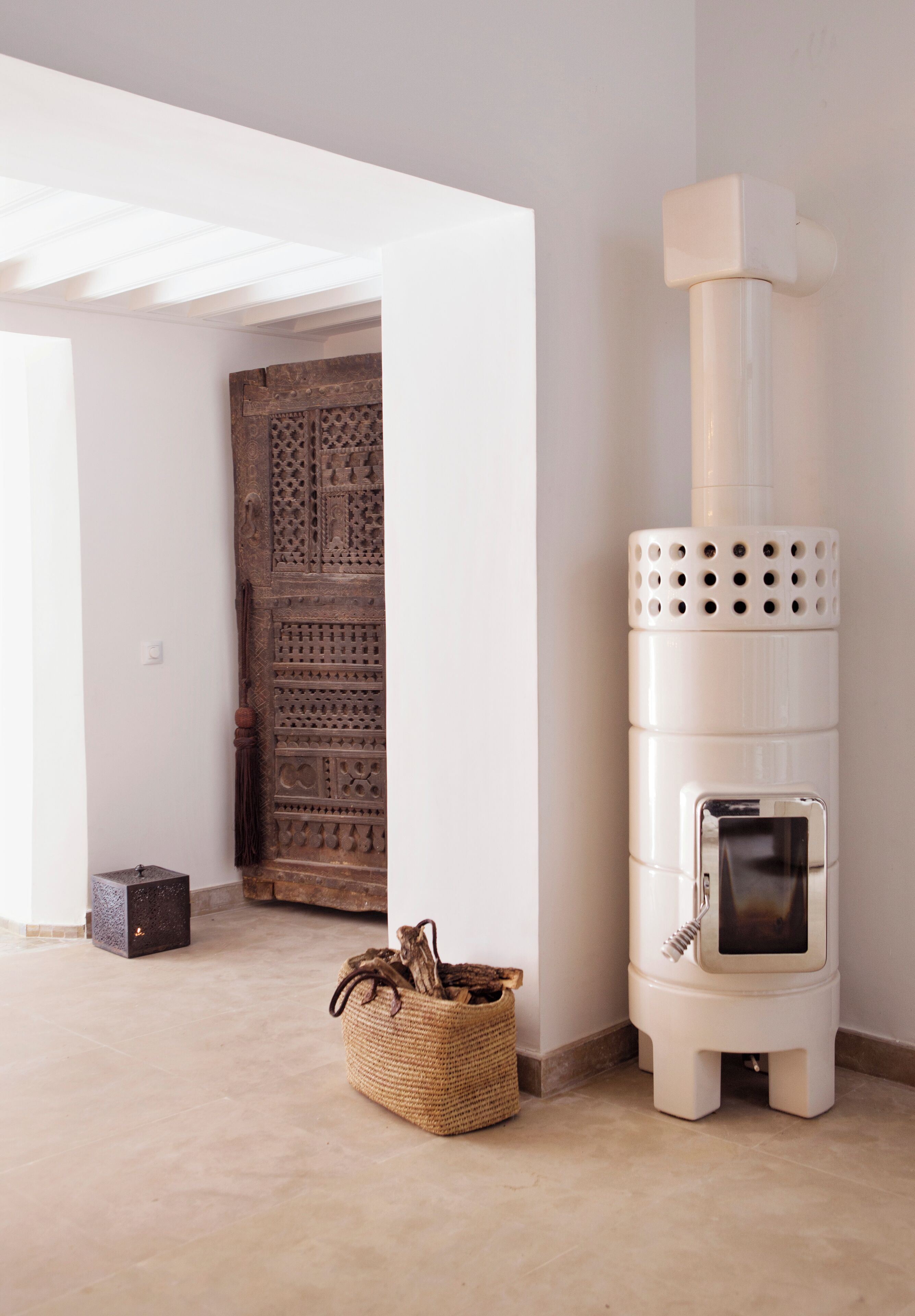 A room with a white wall, a traditional patterned door, a white heater, and a woven basket on the floor.