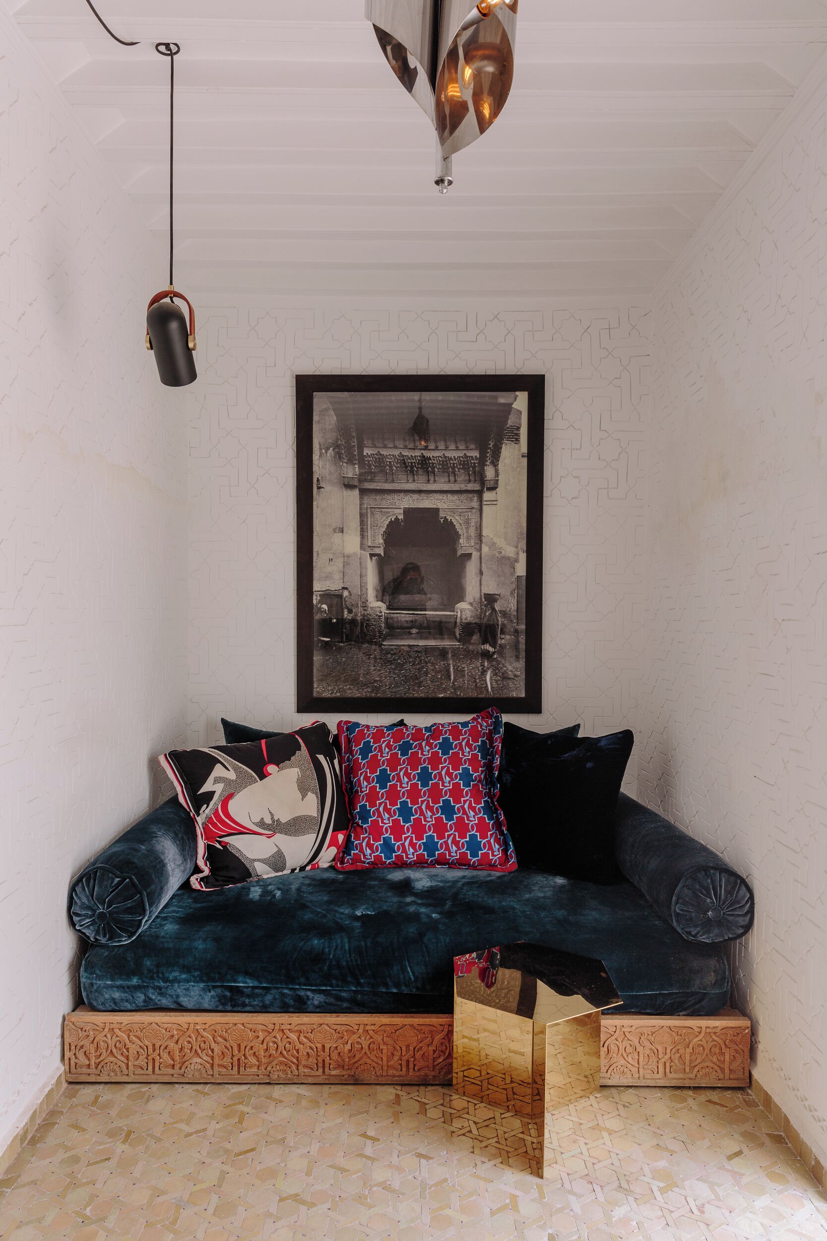 A dark blue velvet sofa with patterned cushions, a framed black and white photograph on the wall, and a hanging pendant light.