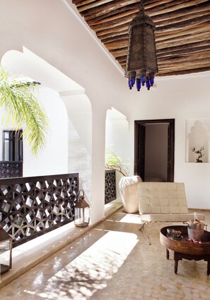 Un intérieur lumineux, avec un mur blanc, un plafond en bois, une lanterne suspendue, un fauteuil rembourré et un sol carrelé.