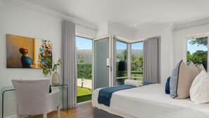 A bedroom with a bed, a chair, a painting, and a view of a garden through a glass door.