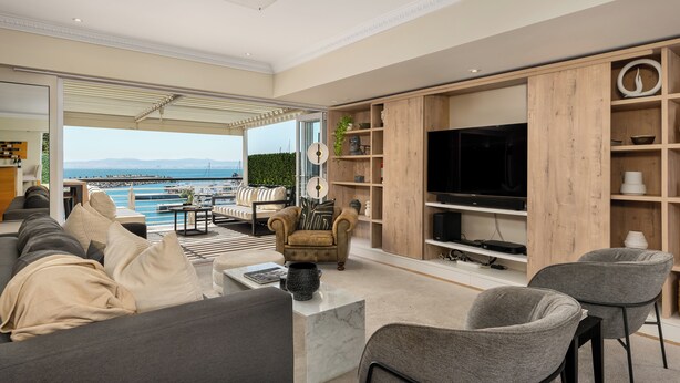A modern living room with a large TV, comfortable seating, and a view of the sea.
