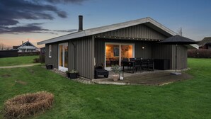 A modern house with a large deck, a chimney, and a well-maintained lawn. - Cozy summer house close to the beach (Assens)