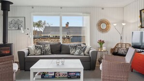 A cozy living room with a sofa, coffee table, and wicker chairs. A fireplace is visible, and there's a TV on a stand. - Cozy summer house close to the beach (Assens)