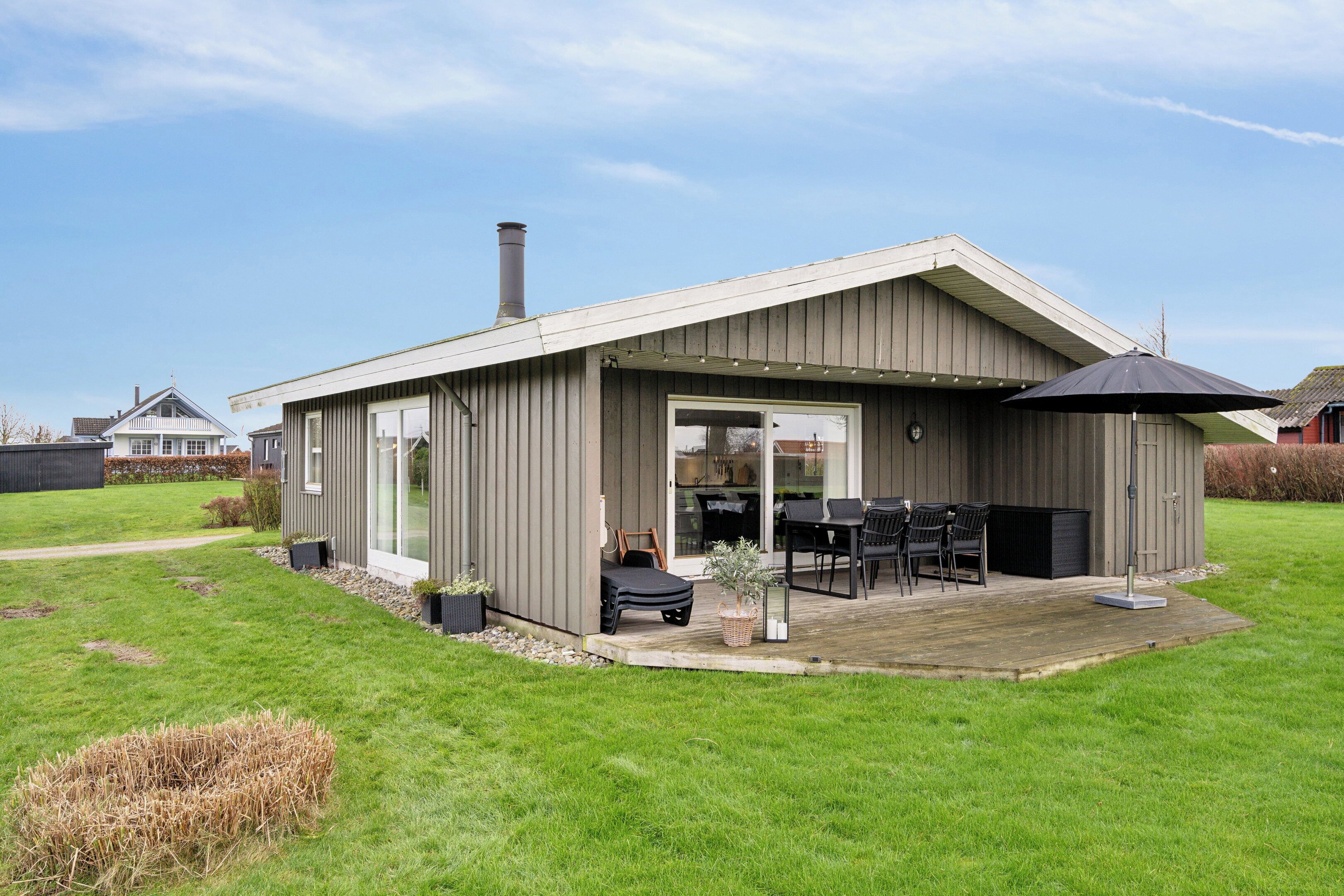 Une maison moderne dotée d’un patio couvert, d’une cheminée et d’une pelouse.