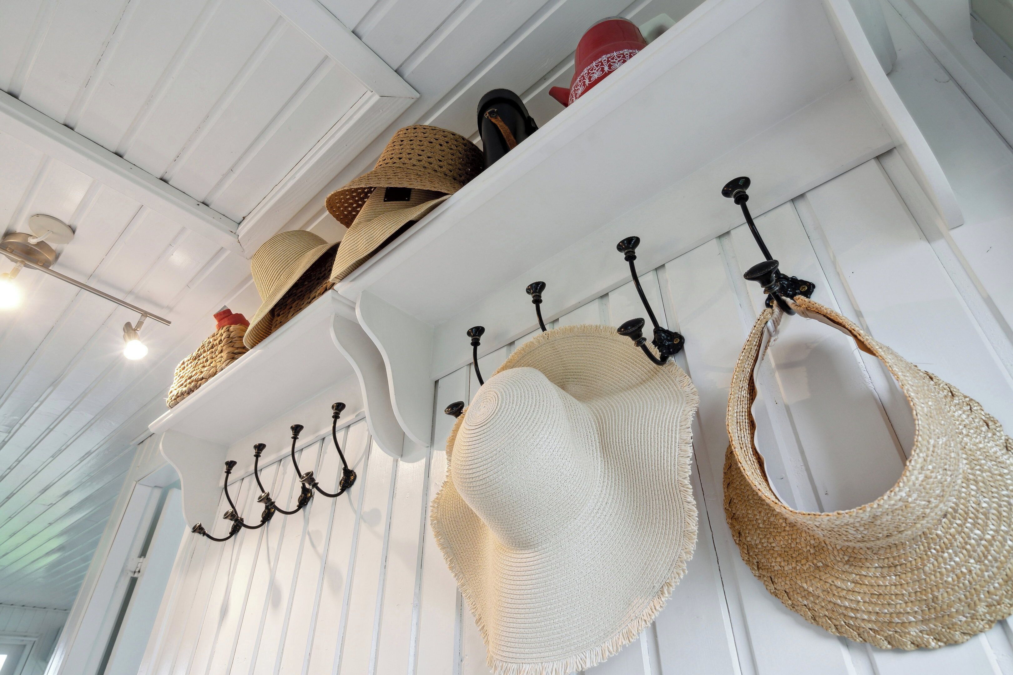 A room with white wooden walls, a ceiling fan, and a shelf with hats and bags.