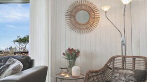 A room with a wicker chair, a round mirror, a vase with flowers, and a table with candles. - Cozy summer house close to the beach (Assens)