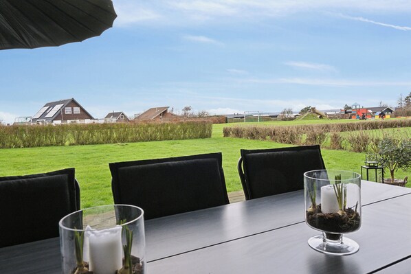 A table with chairs and a glass containing a candle and greenery, set outdoors with a view of houses and a grassy field.