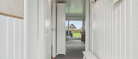 A hallway with a bench, white walls, and a view to an outdoor area.