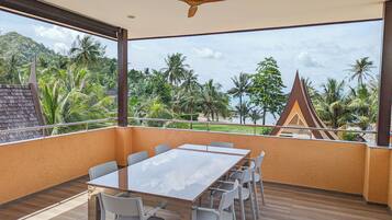 A balcony with a table and chairs, a ceiling fan, and a view of palm trees and a traditional building.