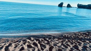 A beach with clear blue water and rocky formations in the distance.