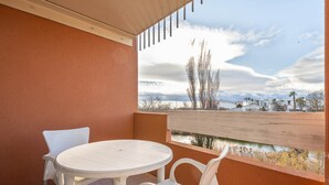 Varanda com mesa redonda e duas cadeiras, dando vista para um corpo d'água e edifícios ao longe.