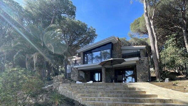 Een modern huis met twee verdiepingen, met stenen trappen die naar een balkon leiden, omringd door bomen.
