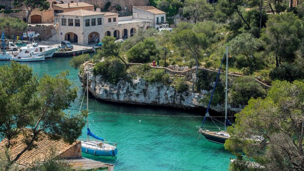 Une ville côtière avec un promontoire rocheux, des eaux turquoise et limpides, et des bateaux amarrés dans le port de plaisance.
