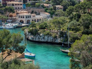 Une ville côtière avec un promontoire rocheux, des eaux turquoise et limpides, et des bateaux amarrés dans le port de plaisance.