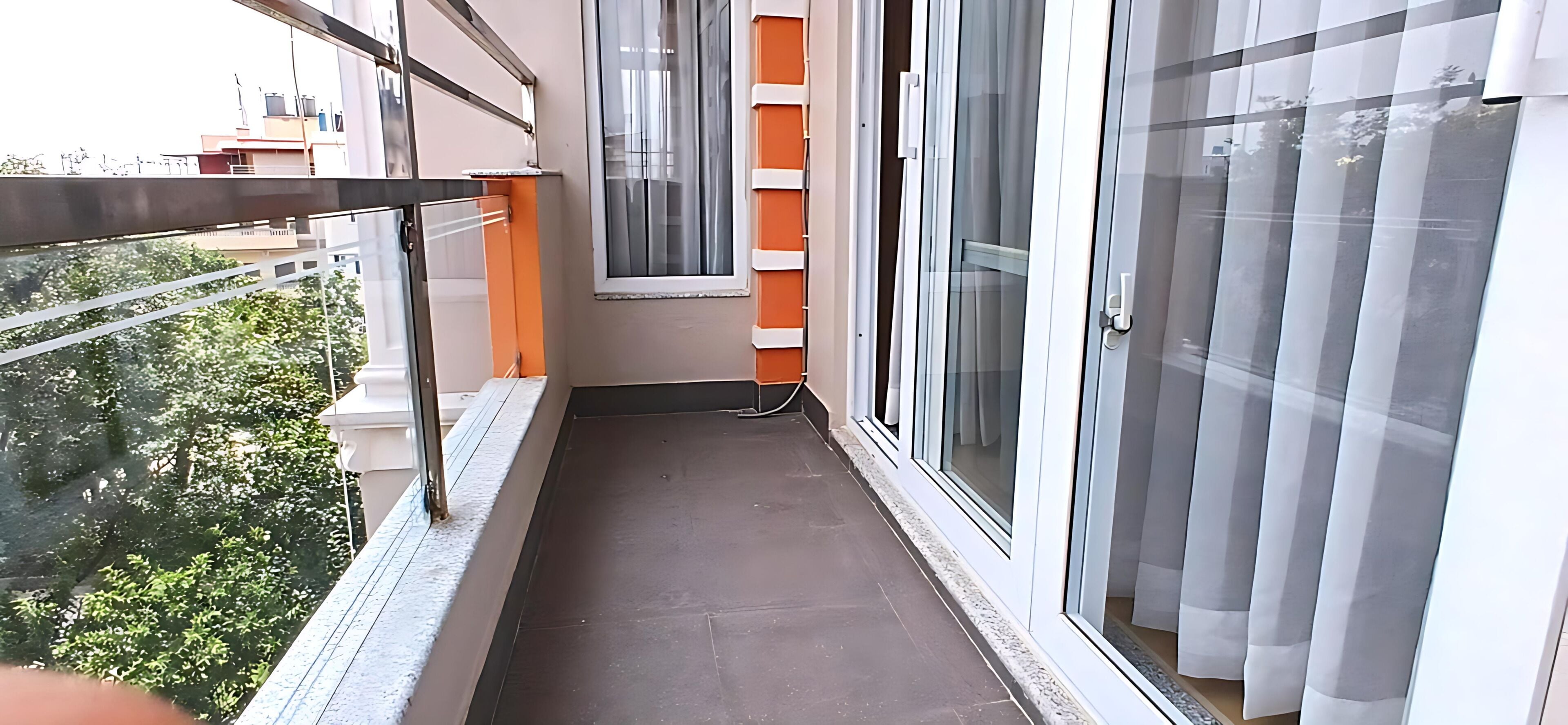 A narrow balcony with a view of trees and buildings.