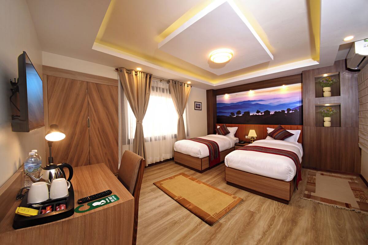 A hotel room with two beds, a desk with a coffee maker, a TV, and a painting of a sunset.