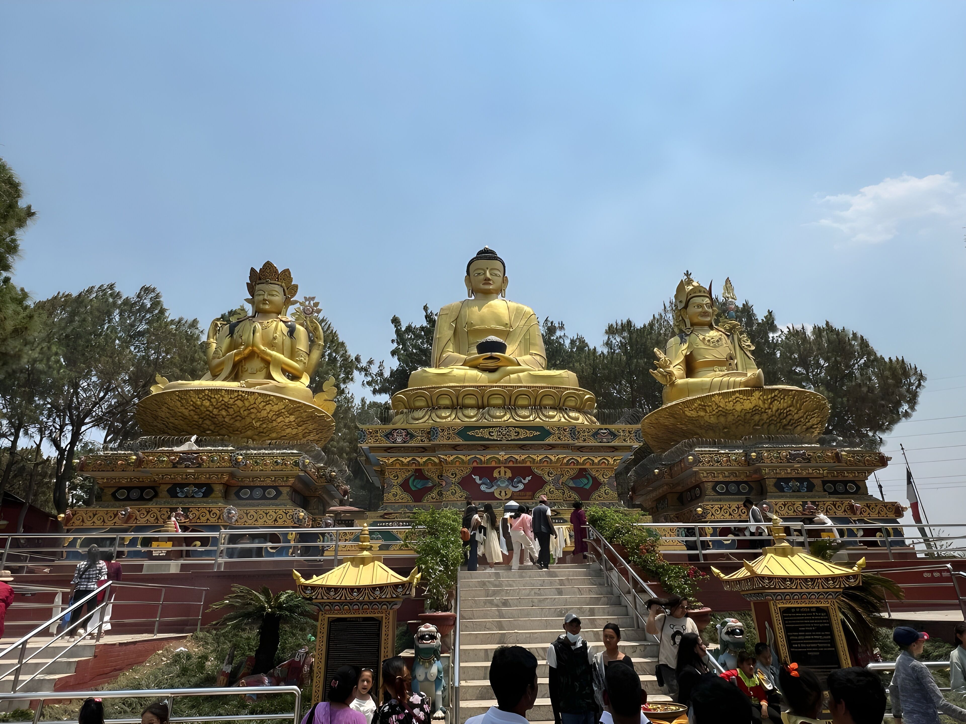 A temple with three golden Buddha statues, stairs leading up to the entrance, and a traditional roof structure.