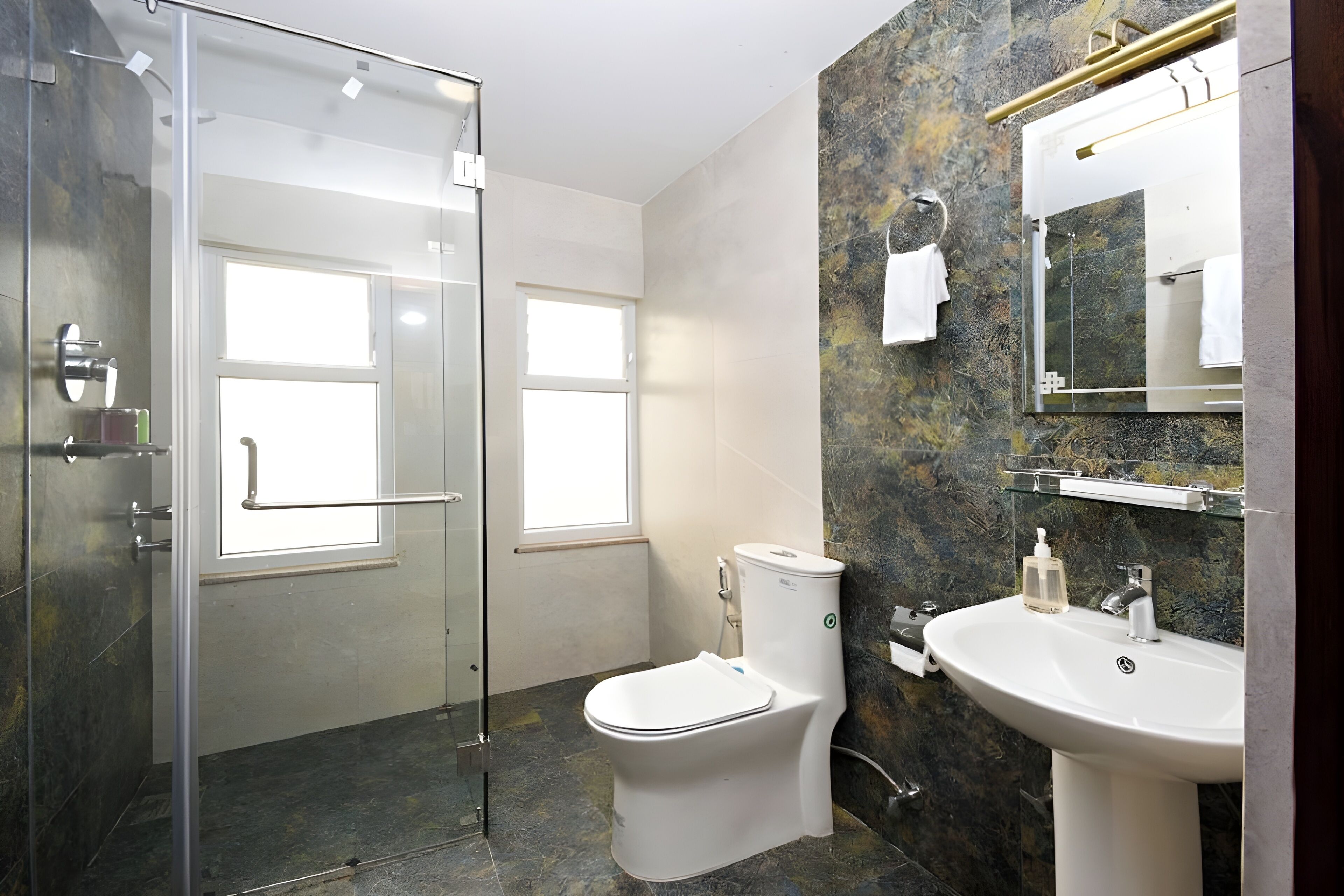 Un baño moderno con ducha envuelta en vidrio, inodoro y lavamanos con frontis de mármol.