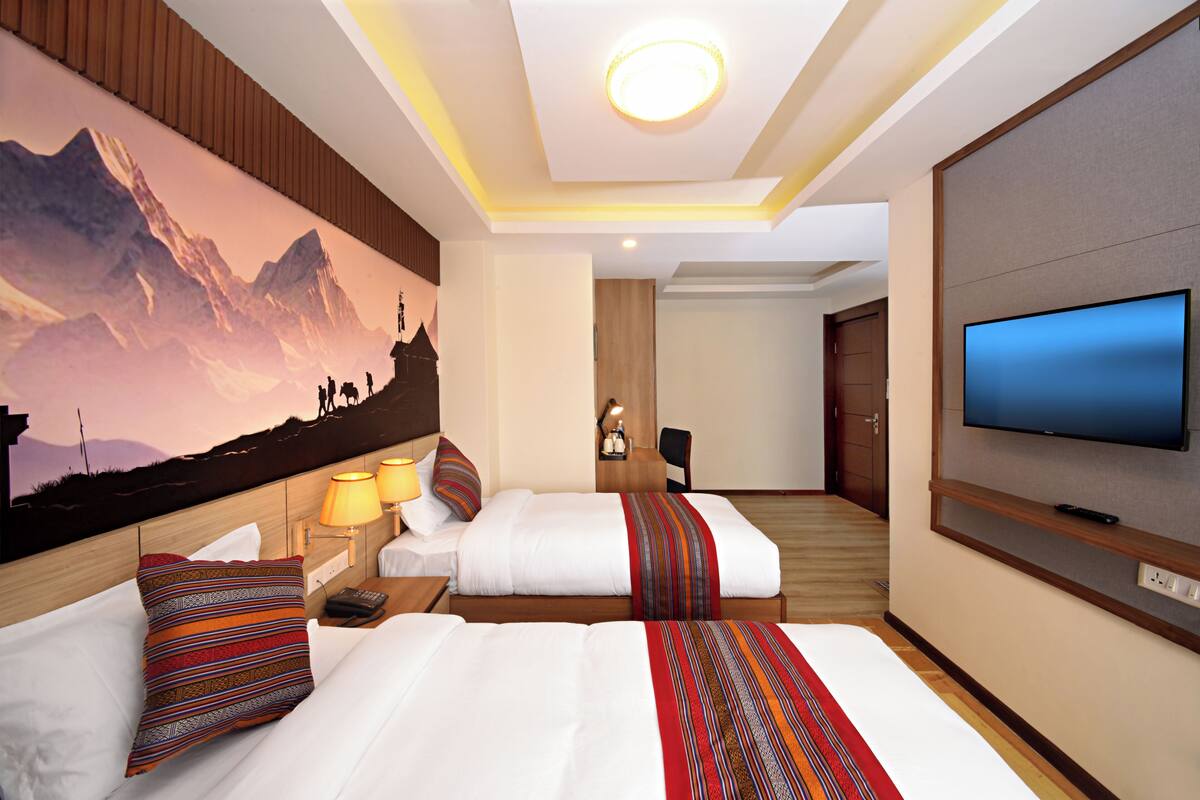A hotel room with two beds, a TV, a painting of mountains, and a wooden ceiling.
