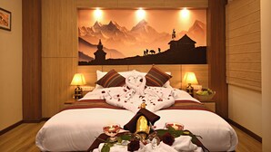 A hotel room with a large bed, two bedside lamps, a wall-mounted air conditioner, and a painting of mountains. - Hotel Sherpani (Kathmandu)