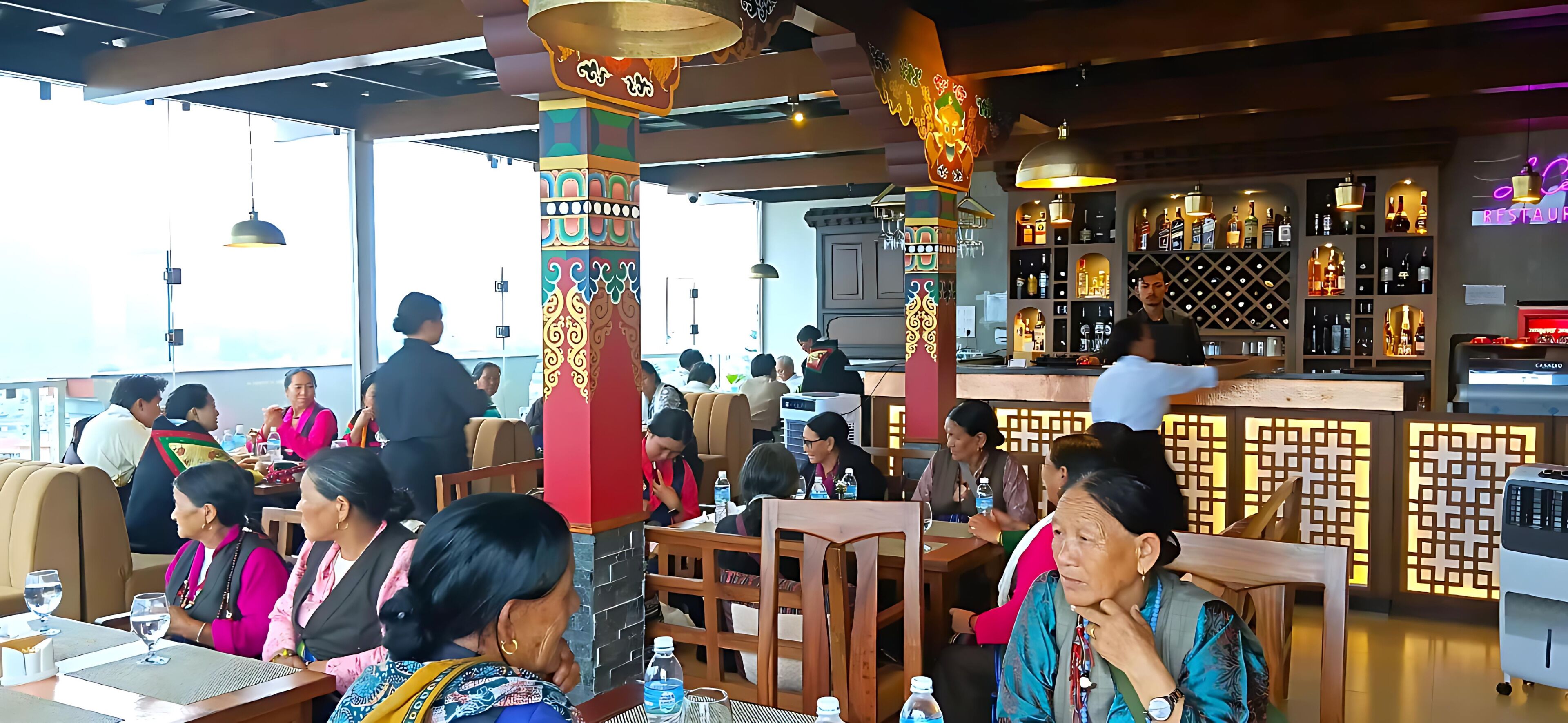 A restaurant with high tables and chairs, a bar area with shelves of bottles, and decorative pillars.