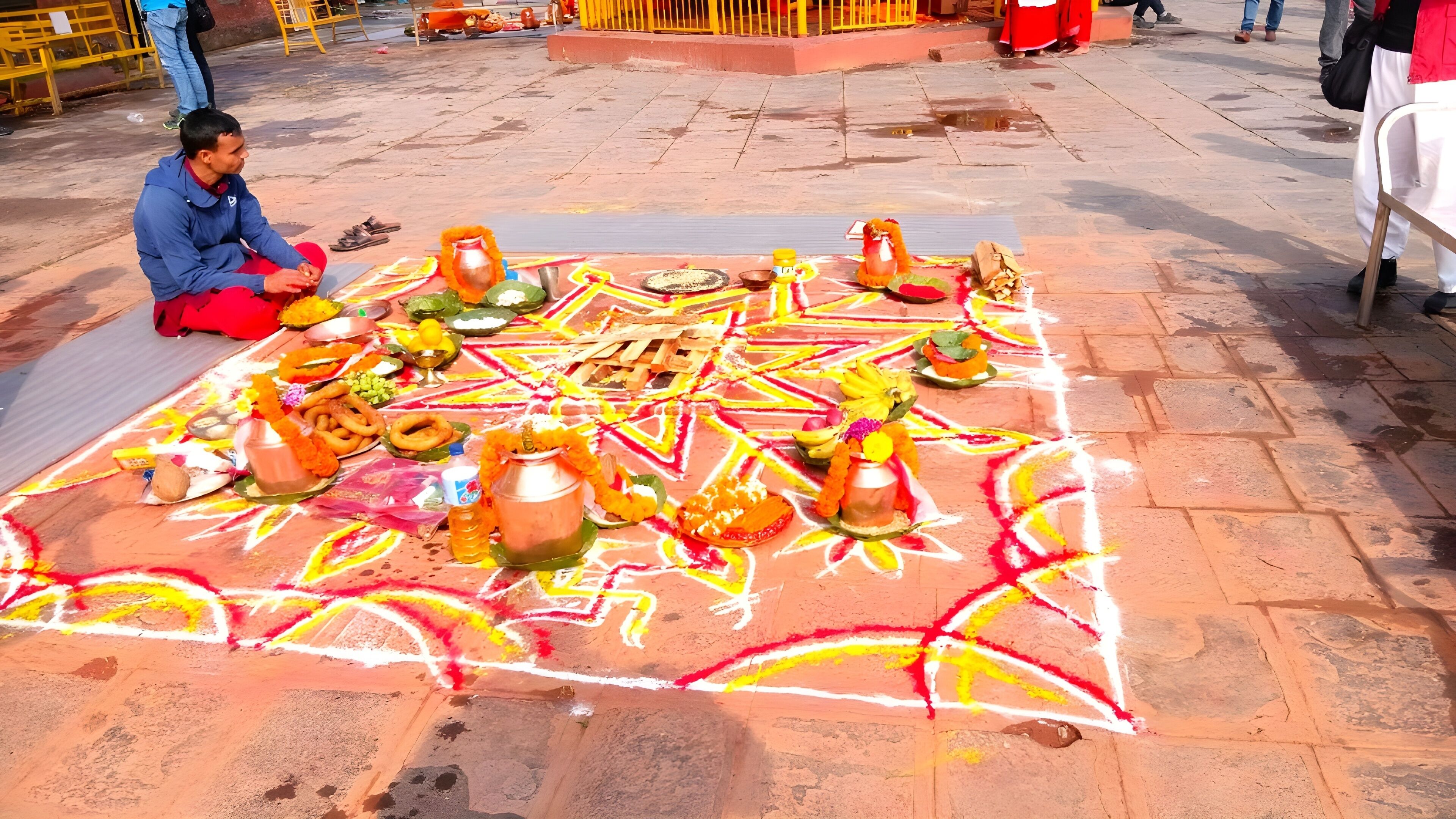 A traditional ceremony with a decorated floor, featuring a person seated and various ritual items.