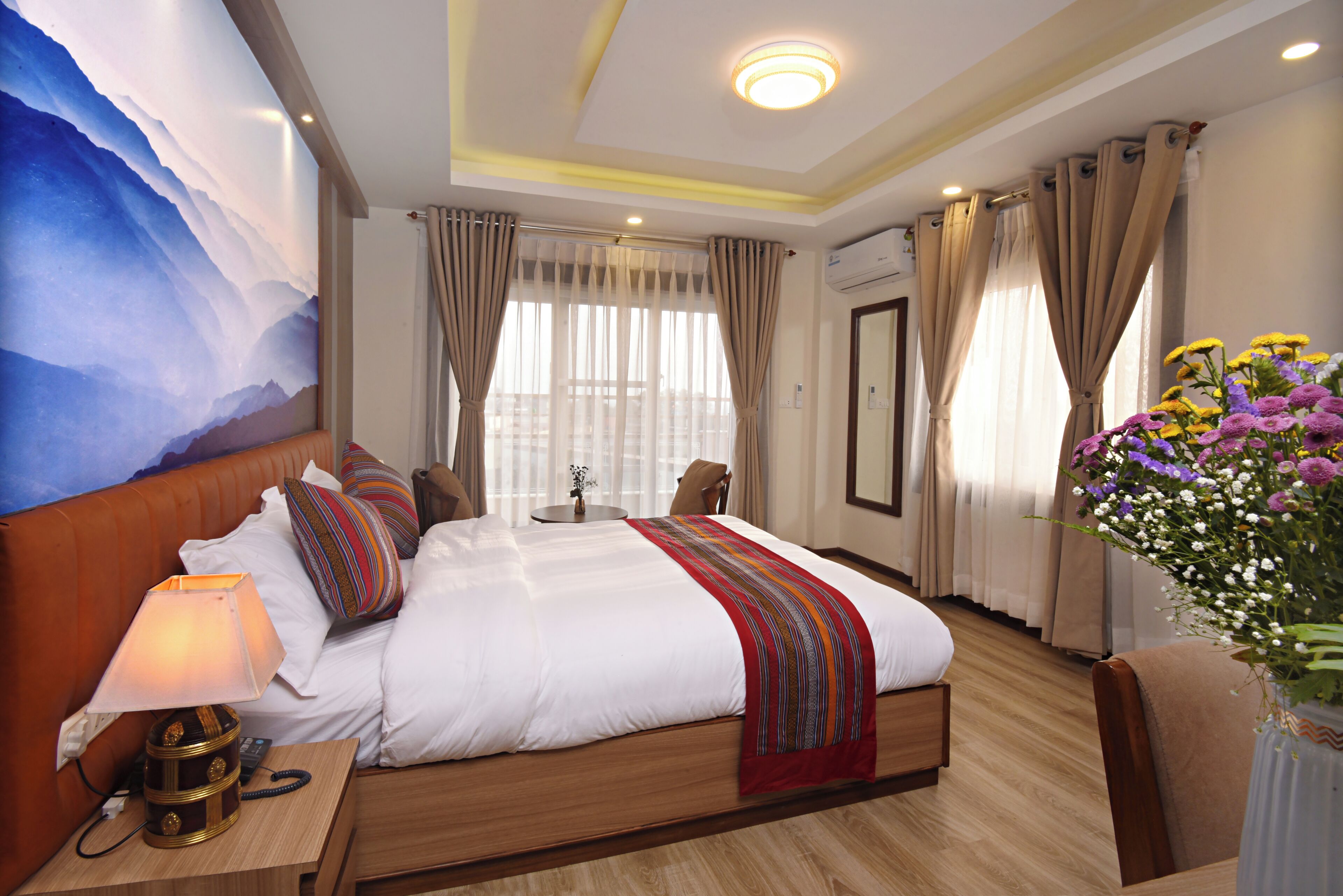 A hotel room with a large bed, a bedside table with a lamp, a vase with flowers, and a painting on the wall.