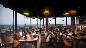 A restaurant with high tables and chairs, large windows, and a view of the city. - Hotel Sherpani (Kathmandu)