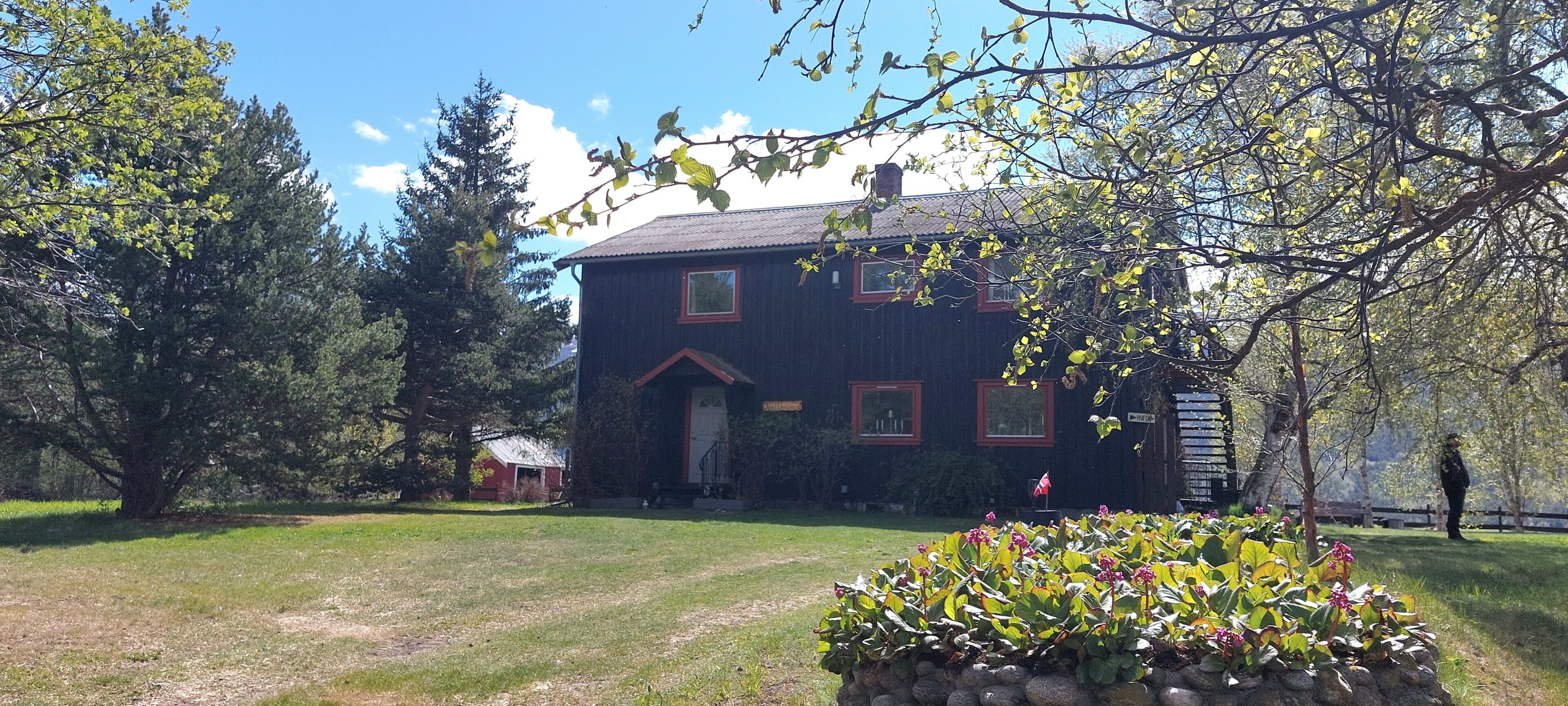 A two-story house with a red door and windows, surrounded by a grassy lawn and trees.