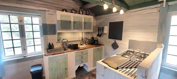 Una cocina rústica con armarios de madera, una estufa a gas y utensilios colgando.