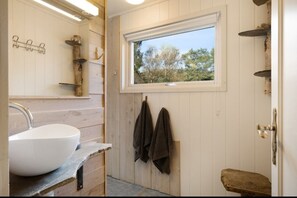 Un baño con un lavamanos blanco, paredes de madera, una ventana y toallas colgadas de ganchos.