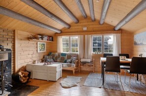 Interior acogedor de una cabaña de troncos con chimenea, un sofá, una mesa de comedor y un ventanal grande.