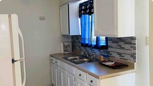 A compact kitchen with white cabinets, a double sink, a microwave, and a tiled backsplash. - 3-bedroom house in beautiful Eagle Pass with WiFi (Eagle Pass)