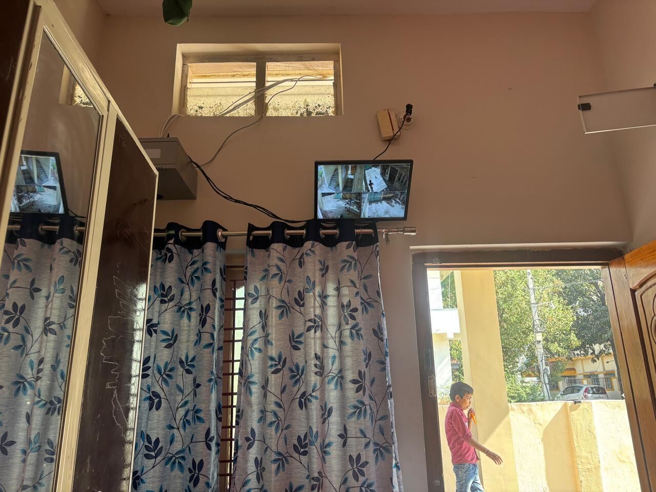 Ein Zimmer mit großem Fenster, einem Vorhang mit Blattmuster und zwei an der Wand befestigten Überwachungskameras.