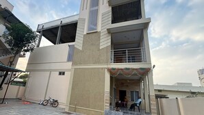 Un edificio residencial de varios pisos con un balcón, una escalera que lleva a la entrada y una bicicleta estacionada afuera.
