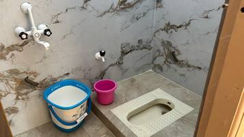 A bathroom with a marble wall, a white toilet, a blue and white bucket, and a pink bucket.
