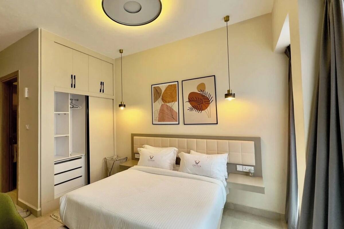 Ein Hotelzimmer mit Bett, Schrank, Nachttisch, Kunstwerk und einer Pendelleuchte.