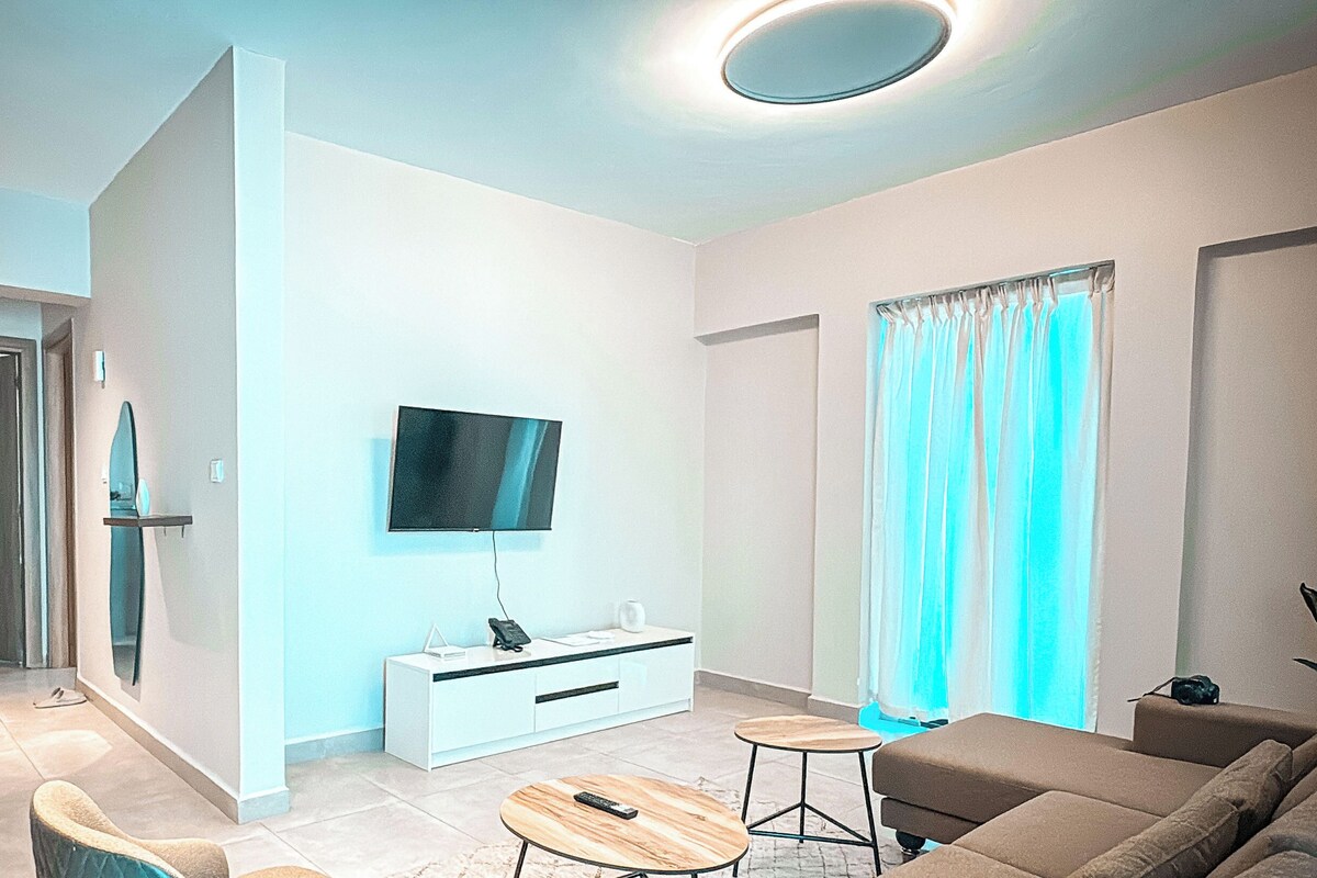 A modern living room with a flat-screen TV, a sofa, a coffee table, and a dining area with a white cabinet.