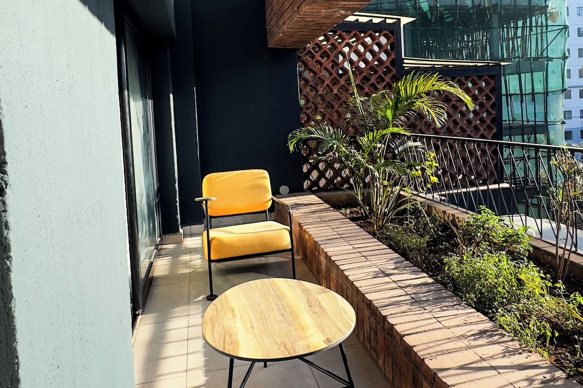 A modern outdoor seating area with a wooden table and chairs, a brick wall, and a view of a building in the background.