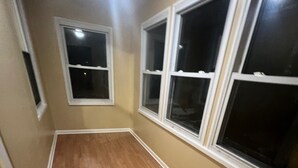 A narrow hallway with wooden flooring and beige walls, featuring three windows with white frames. - Karan Luxury Apartment (Jersey City)