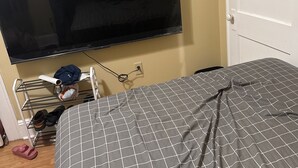 A room with a bed, a TV mounted on the wall, a shoe rack, and a door. - Karan Luxury Apartment (Jersey City)