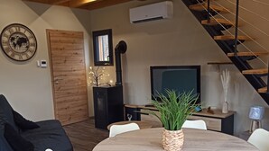 Un salon moderne avec une table ronde en bois entourée de chaises blanches, un canapé noir, un escalier en bois et un grand téléviseur à écran plat.