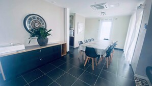 Een moderne eetruimte met een grote tafel, stoelen, een kamerplant en een wandklok.
