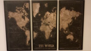 Drie ingekaderde wereldkaarten aan een muur, een biljarttafel op de voorgrond, en een klein rond tafeltje met een zwart object erop.