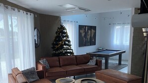 Een moderne woonkamer met een bruine zithoek, twee bijzettafeltjes, een pooltafel en een versierde kerstboom.