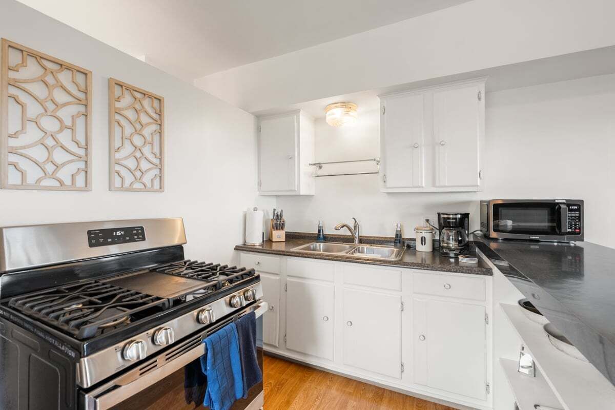 A kitchen with white cabinets, a stainless steel stove, a microwave, and a sink.