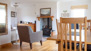 Een eethoek met een houten tafel en stoelen, een gestreept fauteuil, een open haard en een stenen muur.